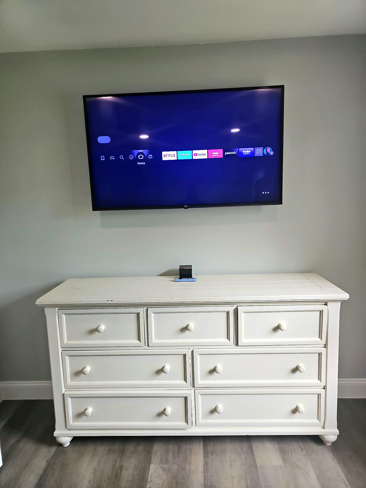 LG TV mounted above a white dresser in a bedroom
